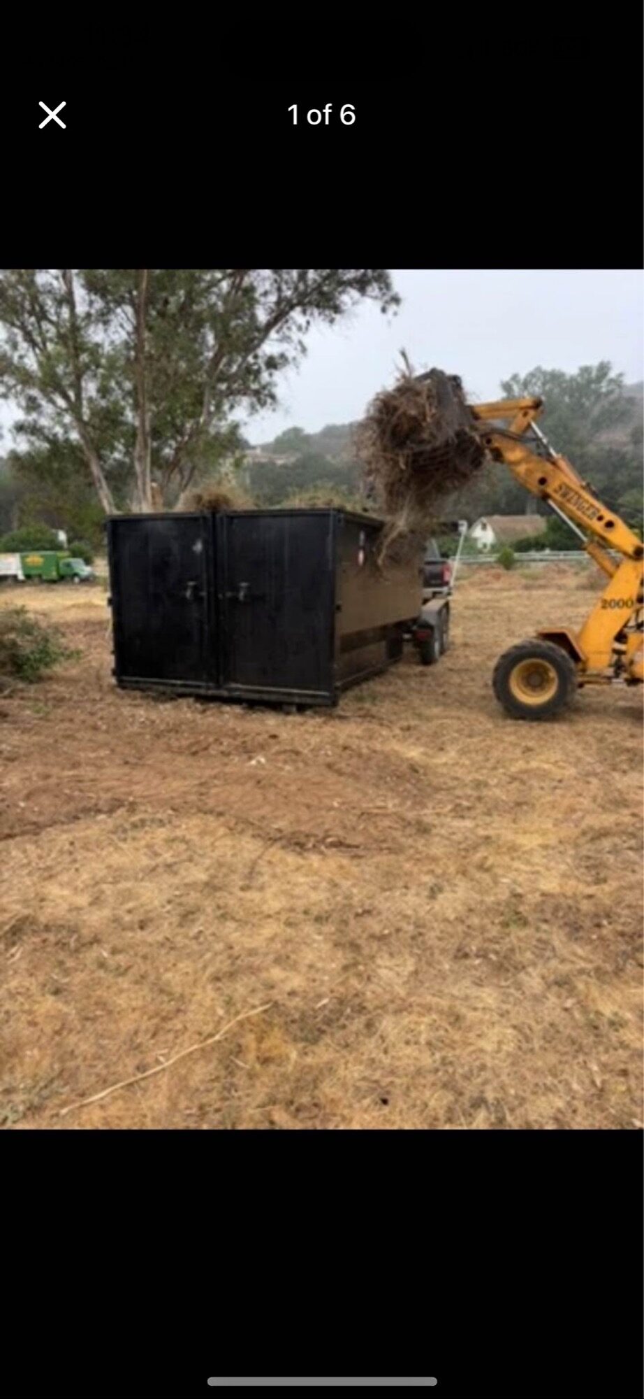 Telehandler loading brush and cleared vegetation into a black OSR dumpster during a land clearing job in Fallbrook